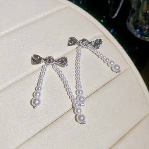 Detailed macro view of elegant silver bow earrings featuring dangling white pearl bead strands