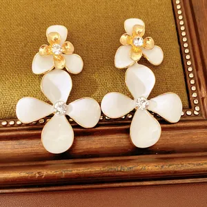 Primo piano di orecchini a fiore in smalto bianco con strass brillanti e dettagli dorati