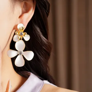Eleganti orecchini a fiore in smalto bianco con strass scintillanti indossati all'orecchio