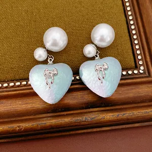 Dettaglio di orecchini cuore perla con fiocco argento su sfondo materico vintage.
