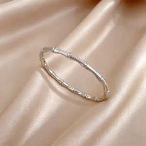 Primer plano de un brazalete rígido de acero de titanio con diseño de bambú sobre seda