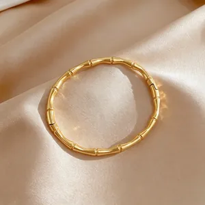 Detalle macro de un brazalete de bambú dorado minimalista sobre tela de satén.