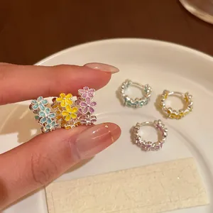 Close-up of delicate floral enamel hoop earrings in blue, yellow, and purple colors.