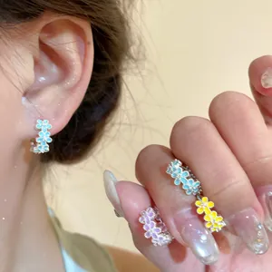 Detailed view of colorful enamel flower huggie earrings worn on ear and held on fingers