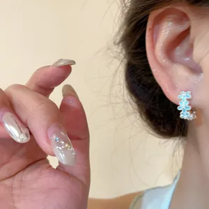 Detailed close-up view of light blue floral enamel hoop earrings worn on a person's ear