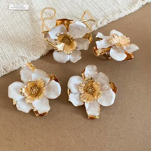 Vista dettagliata di set di gioielli a fiore in metallo dorato con petali in smalto bianco