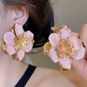 Dettaglio di grandi orecchini a fiore in smalto rosa con centro in metallo dorato