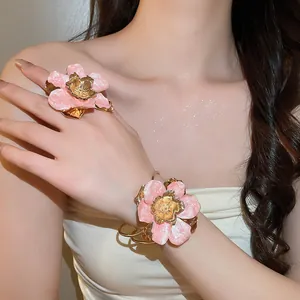 Dettaglio di un set di anello e bracciale a fiore in smalto rosa sulla mano di una modella.