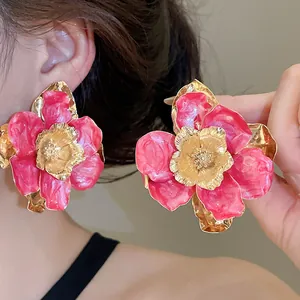 Dettaglio di orecchini a fiore in smalto rosa con petali dorati stropicciati