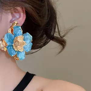 Primo piano dettagliato di un grande orecchino a fiore blu e oro indossato da una modella.