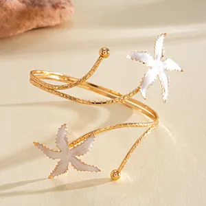Detail van een stijlvolle gouden bovenarmband met witte geëmailleerde zeesterren