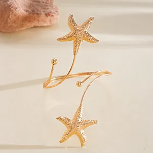 Detailweergave van een goudkleurige armring met getextureerde zeestervormige bedeltjes.