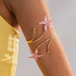 Detailweergave van een goudkleurige zeester-armband met roze emaille om de arm