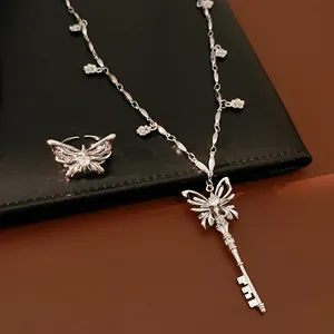 Detailed view of a silver butterfly key necklace and ring set on leather background.