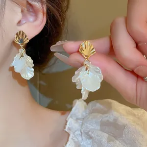 Vista detallada de elegantes pendientes de concha dorados con pétalos blancos translúcidos