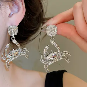 Close-up detail of oversized silver crab drop earrings featuring textured studs and crystal accents