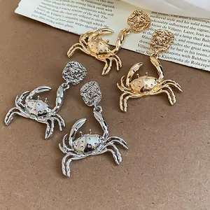 Detailed close-up of golden and silver crab-shaped earrings with intricate metallic textures.
