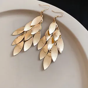 Elegant gold metal leaf tassel hook earrings with a brushed finish on a neutral plate