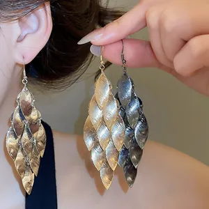 Detailed close-up of layered metallic leaf tassel earrings in gold, silver, and black.