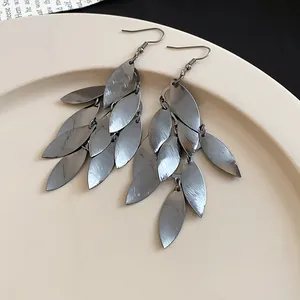 Close-up of gunmetal grey metal leaf tassel earrings with brushed texture on cream plate.
