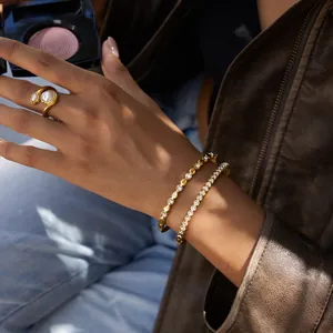 Détail de joncs dorés avec diamants et une bague perles sur la main d'un mannequin