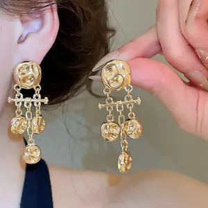 Detailed view of gold hammered metallic tassel earrings worn on ear and held by hand
