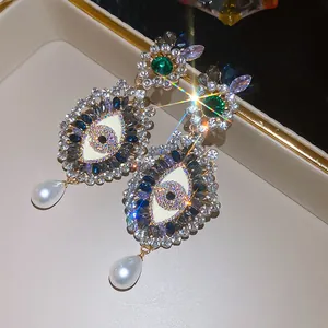 Detailed macro view of vintage rhinestone evil eye earrings with teardrop pearl pendants