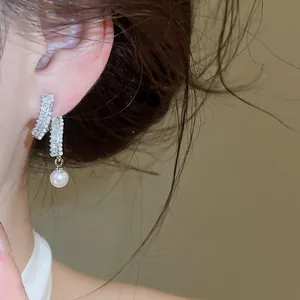 Close-up detail of elegant silver earrings featuring sparkling zirconia and a hanging pearl
