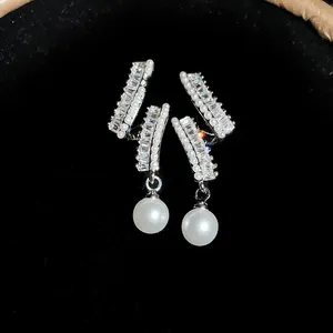 Close-up of elegant luxury drop earrings with baguette zircons and pendant pearls on black