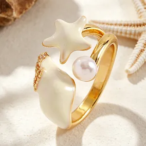 Primer plano anillo dorado con estrella de mar, caracola esmaltada y perla