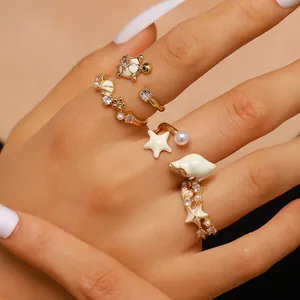 Detalle de anillos dorados de tortuga, estrella de mar y concha con esmalte blanco y circonitas