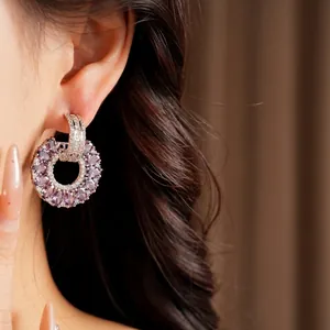 Elegantes pendientes redondos huecos con circón púrpura en una bella modelo asiática