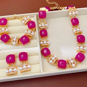 Vista detallada de un conjunto de joyas vintage con piedras magenta y perlas en una bandeja.