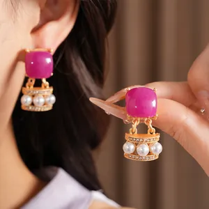 Vista macro detallada de pendientes vintage dorados con piedra magenta y perlas elegantes