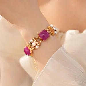 Vista detallada de una pulsera vintage de oro con piedras púrpuras y perlas en la muñeca