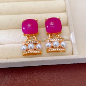 Detalle de pendientes vintage dorados con cuadrados magenta y perlas elegantes.
