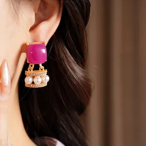 Detalle de primer plano de pendientes vintage dorados con piedra magenta y perlas