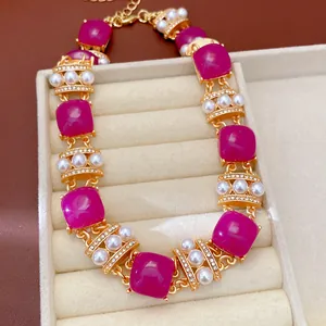 Vista macro detallada de collar vintage dorado con piedras cuadradas magenta y perlas.