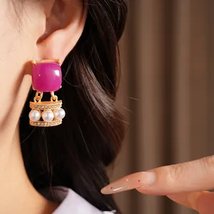 Primer plano de pendientes vintage dorados con piedra magenta y perlas blancas