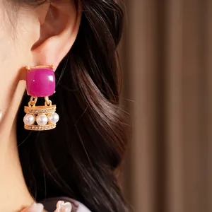 Primer plano de pendientes vintage con piedra magenta, perlas blancas y cristales