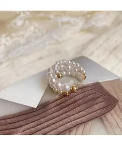 Λεπτομερής κοντινή λήψη ενός κομψού ear cuff με λευκές πέρλες και χρυσό φινίρισμα.