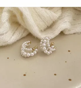 Κοντινό πλάνο από πέρλες ear cuffs σε στρώσεις με χρυσές λεπτομέρειες σε κρεμ ύφασμα