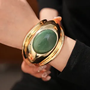 Bold chunky gold-tone cuff bracelet featuring a large oval green gemstone centerpiece