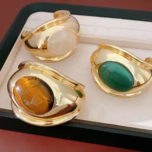 Detail view of bold gold twisted bangles with oval tiger eye and green stones