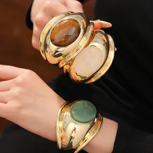 Detailed view of chunky gold cuffs with tiger's eye and green aventurine stones.
