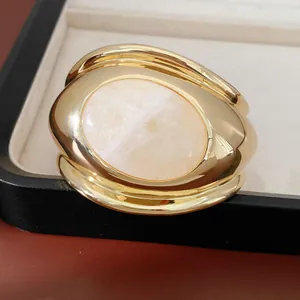 Close-up of twisted gold cuff bracelet with large oval pink rose quartz stone inlay.