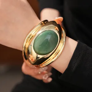 Detailed close-up of a bold gold-toned cuff bracelet with a large oval green gemstone.