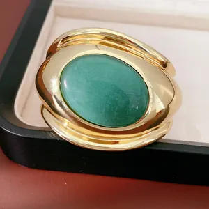 Close-up view of a chunky gold open cuff bracelet featuring a large green oval stone
