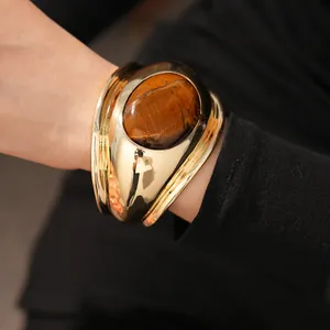 Close-up of a bold gold-toned cuff bracelet featuring a large oval tiger's eye stone.