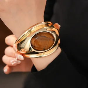 Close-up detail of a twisted gold cuff bracelet with a large oval tiger's eye stone